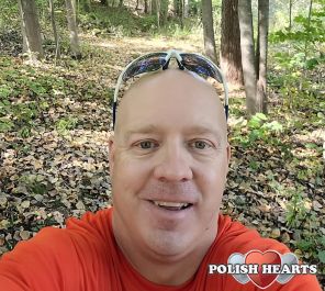 The photograph captures a serene forest setting, featuring a sunlit trail surrounded by trees adorned with vibrant green leaves. The ground is covered with a mix of fallen leaves, adding a touch of autumnal beauty to the scene. 